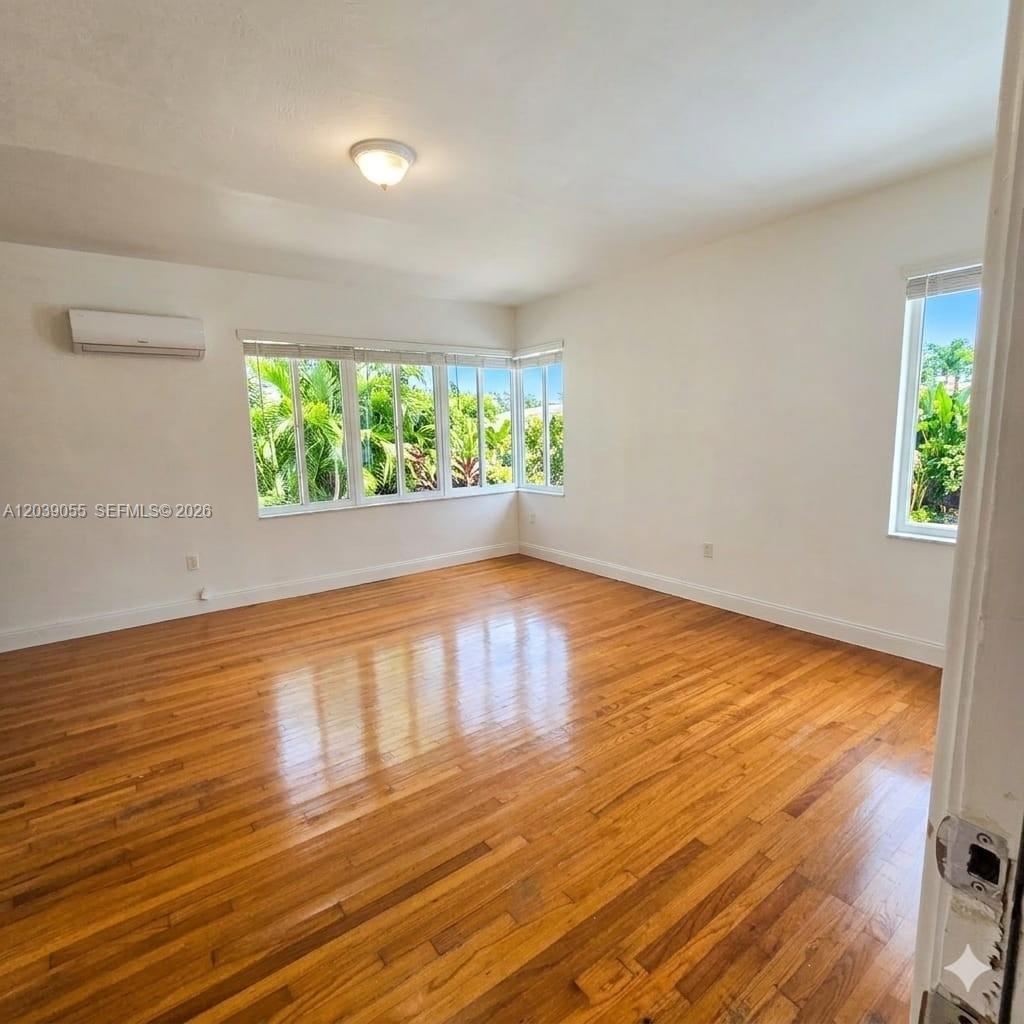 An empty room features hardwood floors, white walls, a corner window, and a wall-mounted AC — 7936 Harding Ave # 5, Miami Beach FL 33141, MIAMI BEACH, FL