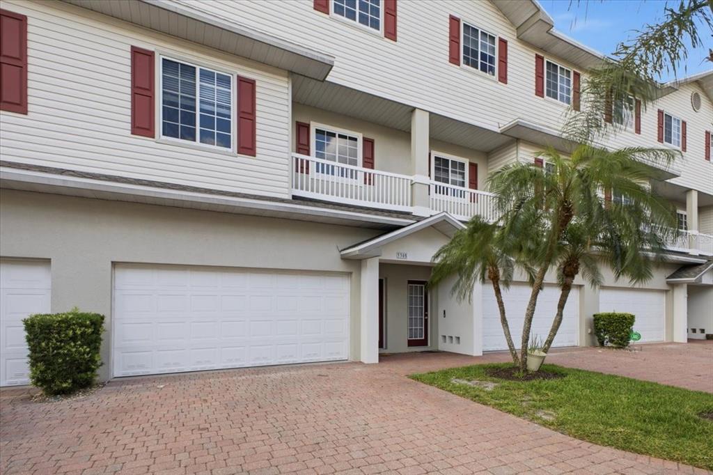 A multi-story townhouse exterior with a brick paver driveway, white garage doors, and red shutters — 3305 10TH LANE W, PALMETTO, FL
