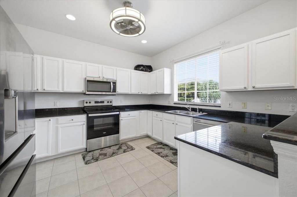 A kitchen with white cabinets, black countertops, stainless steel appliances, and light tile flooring — 3305 10TH LANE W, PALMETTO, FL