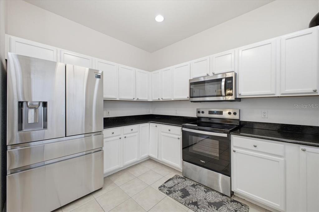 A kitchen features white cabinets, black countertops, stainless steel appliances, and light-colored tile flooring — 3305 10TH LANE W, PALMETTO, FL