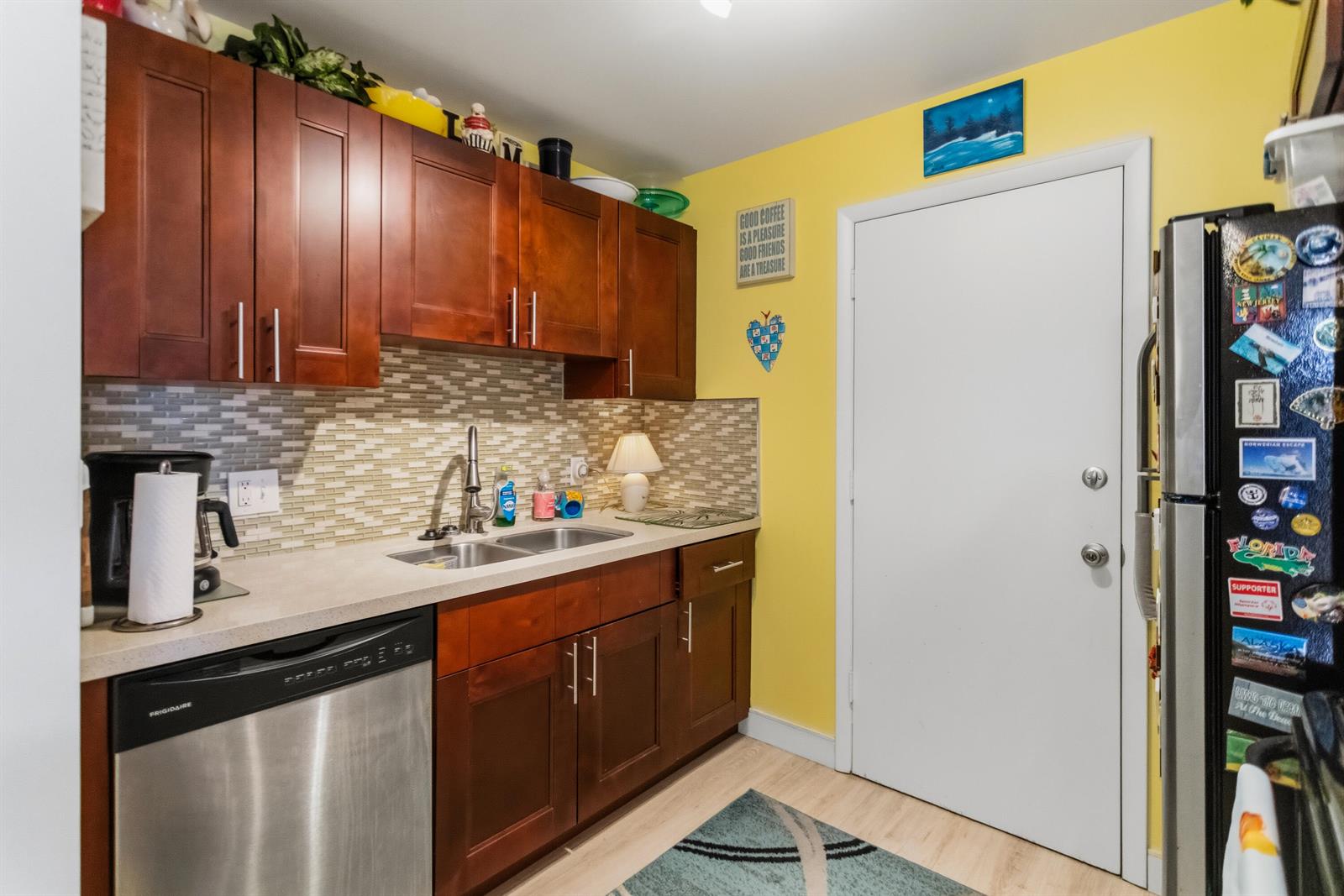 A kitchen featuring dark wood cabinets, stainless steel appliances, a tiled backsplash, and yellow walls — 101 E Mcnab Road # 408, Pompano Beach FL 33060, POMPANO BEACH, FL