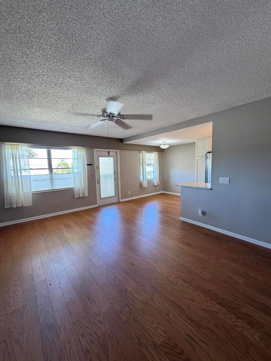 An open-concept living area features wood flooring, a ceiling fan, and an adjacent kitchen counter — 166 Dorset D, Boca Raton FL 33434, BOCA RATON, FL