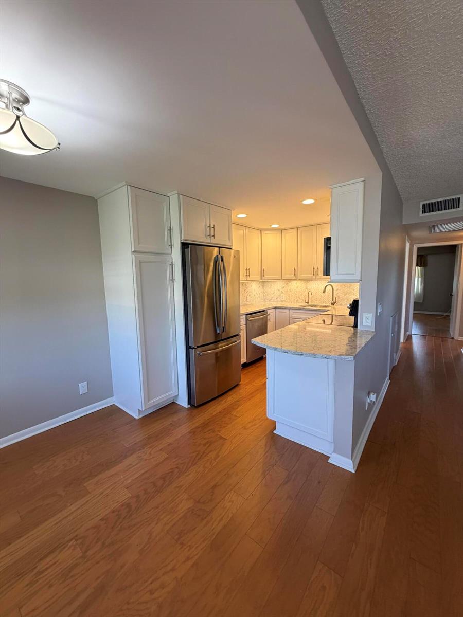 A kitchen with white cabinets, stainless steel appliances, and granite countertops over hardwood floors — 166 Dorset D, Boca Raton FL 33434, BOCA RATON, FL