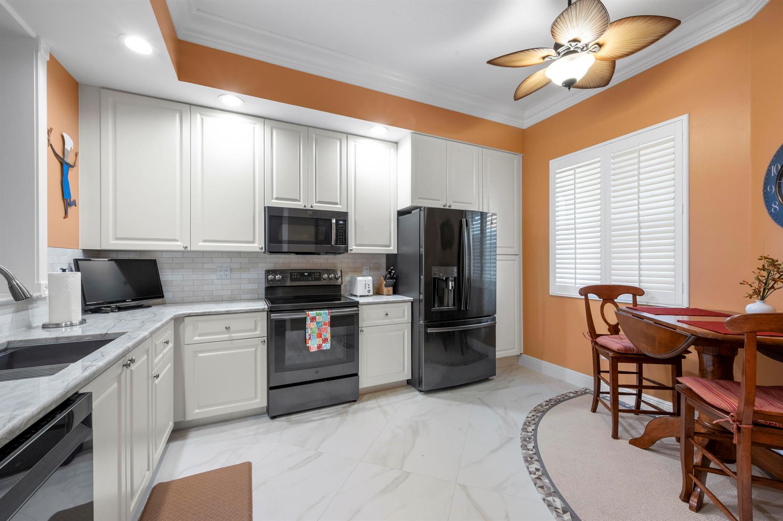 A kitchen with white cabinets, black appliances, marble countertops, and a small dining area — 8 Harbour Isle Drive E, Fort Pierce FL 34949, FORT PIERCE, FL