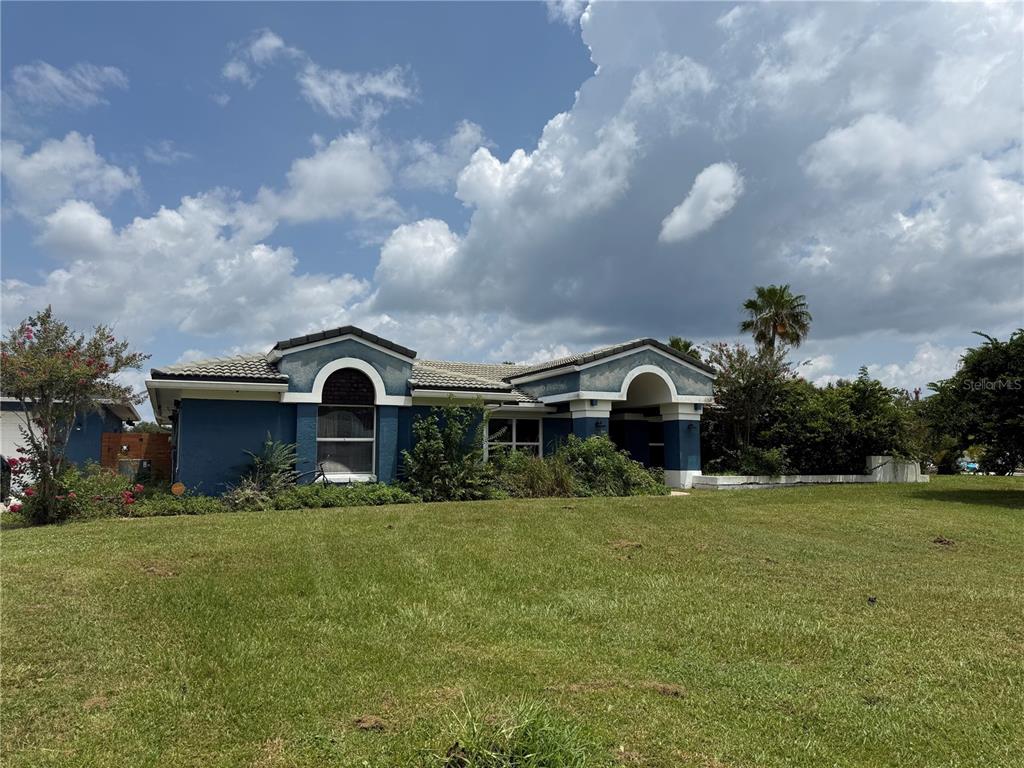 A blue, single-story house with arched architectural details sits on a large, grassy lawn — 2749 S STEWART STREET, KISSIMMEE, FL
