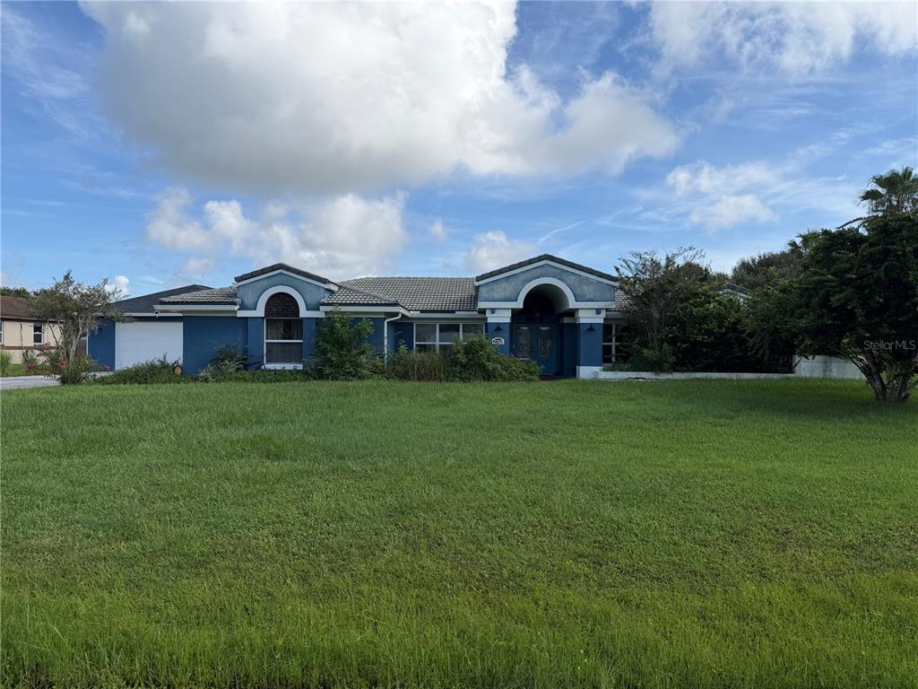 A blue single-story house with a large front lawn under a partly cloudy sky — 2749 S STEWART STREET, KISSIMMEE, FL
