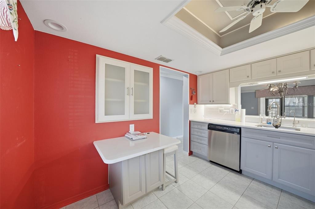 A kitchen features a red accent wall, light gray cabinets, a white island, and tile flooring — 2130 ELM STREET UNIT 401, DUNEDIN, FL