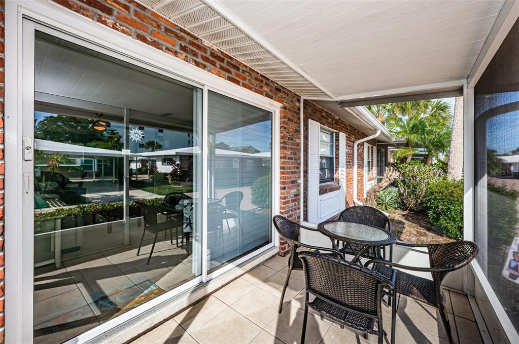 A covered patio features tiled flooring, a brick wall, and a small table with chairs — 6020 MIDNIGHT PASS ROAD UNIT 14A, SARASOTA, FL