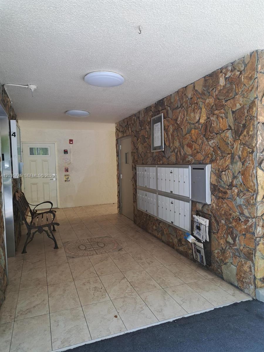 An indoor building lobby features a stone wall, mailboxes, tiled flooring, and a bench — 1024 SE 3rd Ave # 304, Dania Beach FL 33004, DANIA BEACH, FL