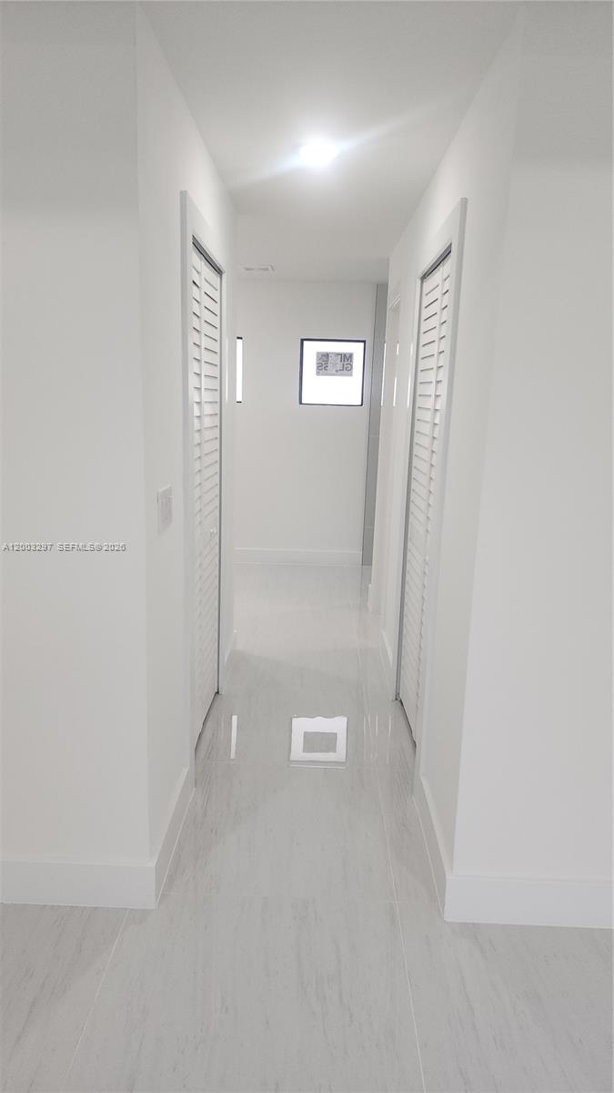 A narrow white hallway features light-colored tile flooring and louvered closet doors on both sides — 2615 40th ST W, Lehigh Acres FL 33971, LEHIGH ACRES, FL