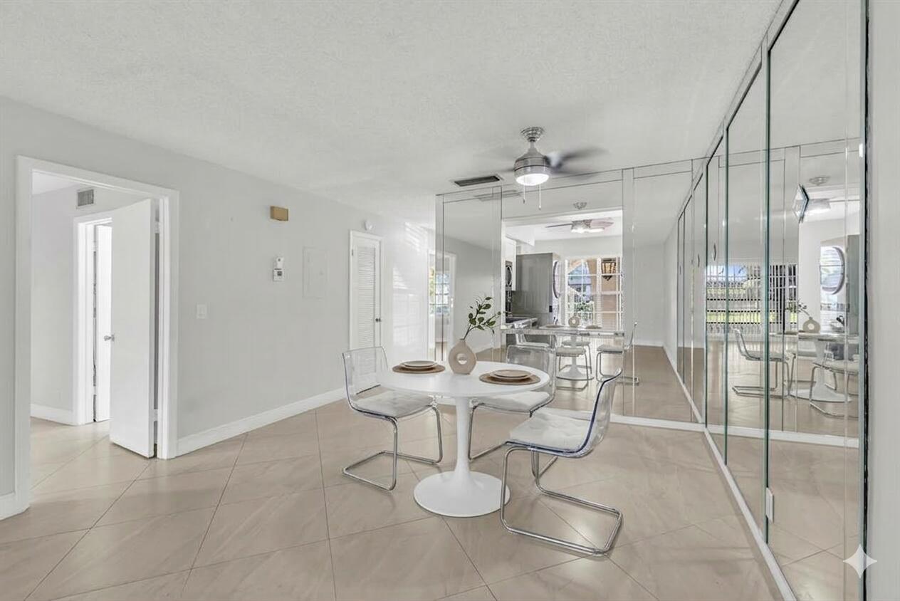 A dining area with a white pedestal table, clear chairs, tile floors, and mirrored walls — 13950 Via Flora # B, Delray Beach FL 33484, DELRAY BEACH, FL