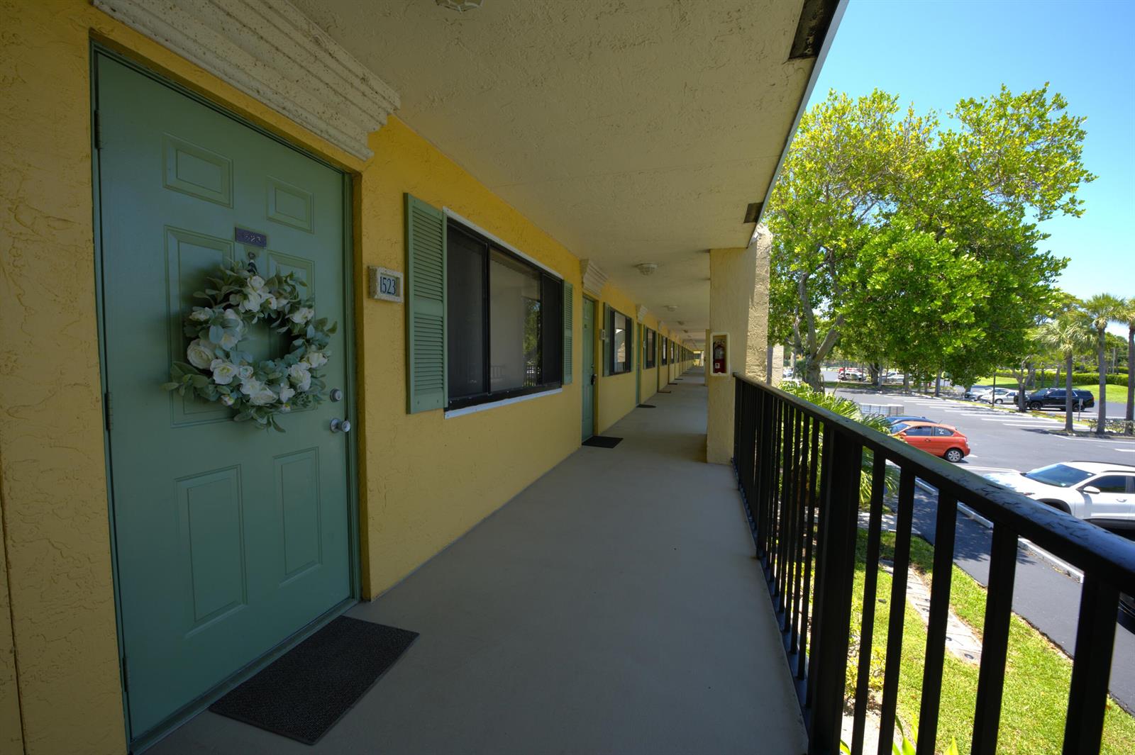 An exterior walkway with yellow walls, green doors, and a black metal railing overlooks a parking lot — 1523 Meadows Circle W, Boynton Beach FL 33436, BOYNTON BEACH, FL