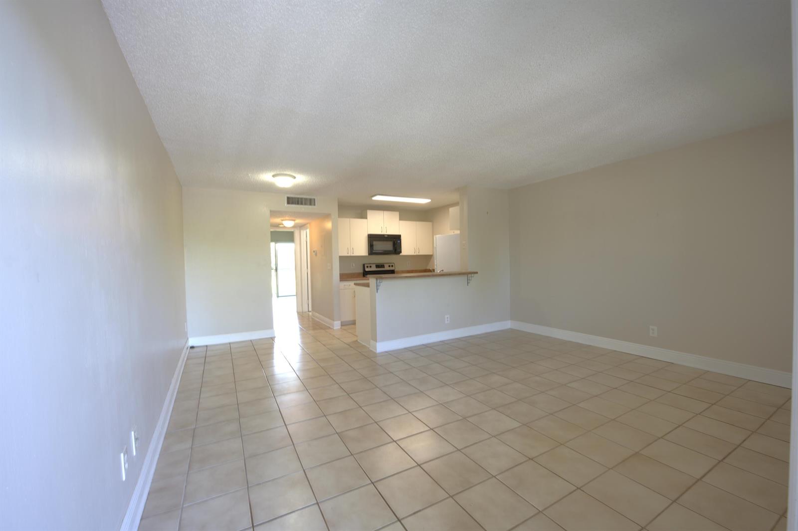 An open-concept living area with tile flooring leads to a kitchen with white cabinets — 1523 Meadows Circle W, Boynton Beach FL 33436, BOYNTON BEACH, FL