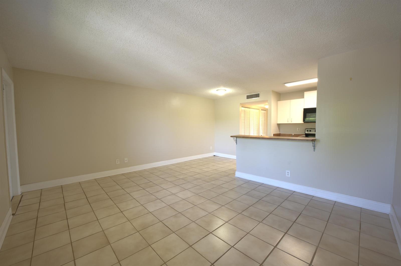 An empty living room with beige tile flooring, neutral walls, and an open kitchen pass-through — 1523 Meadows Circle W, Boynton Beach FL 33436, BOYNTON BEACH, FL
