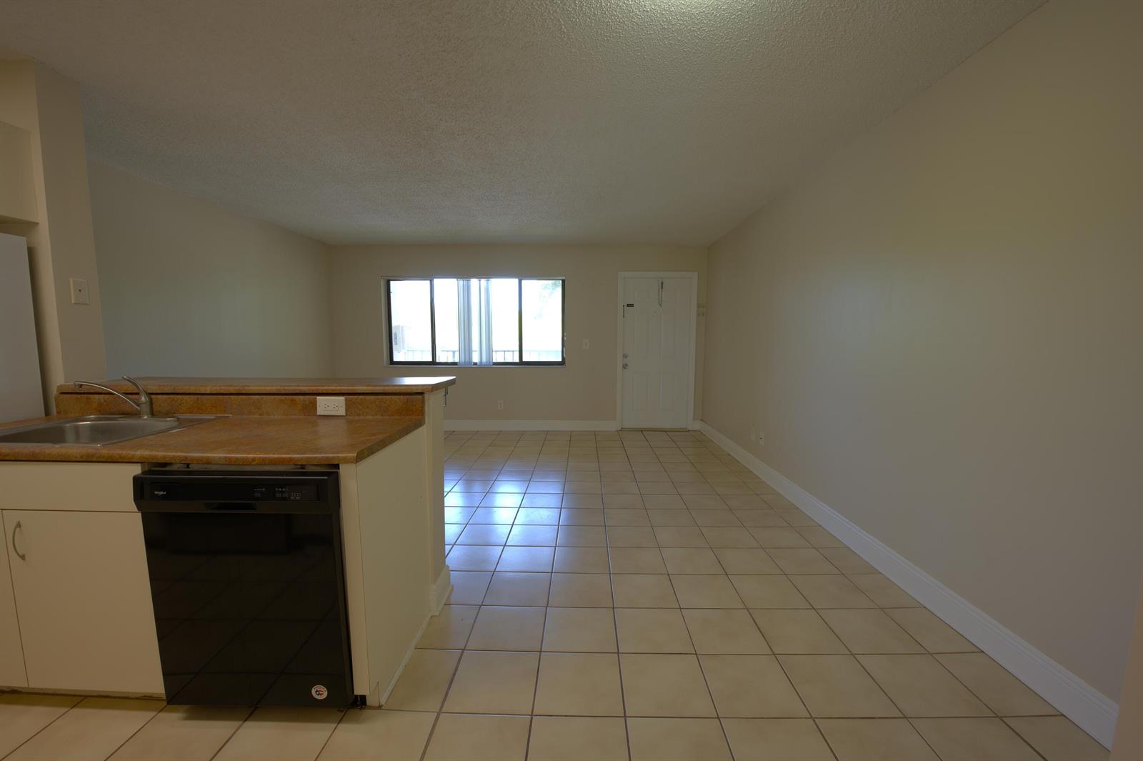 A kitchen counter with a black dishwasher overlooks an open living area with tiled floors — 1523 Meadows Circle W, Boynton Beach FL 33436, BOYNTON BEACH, FL