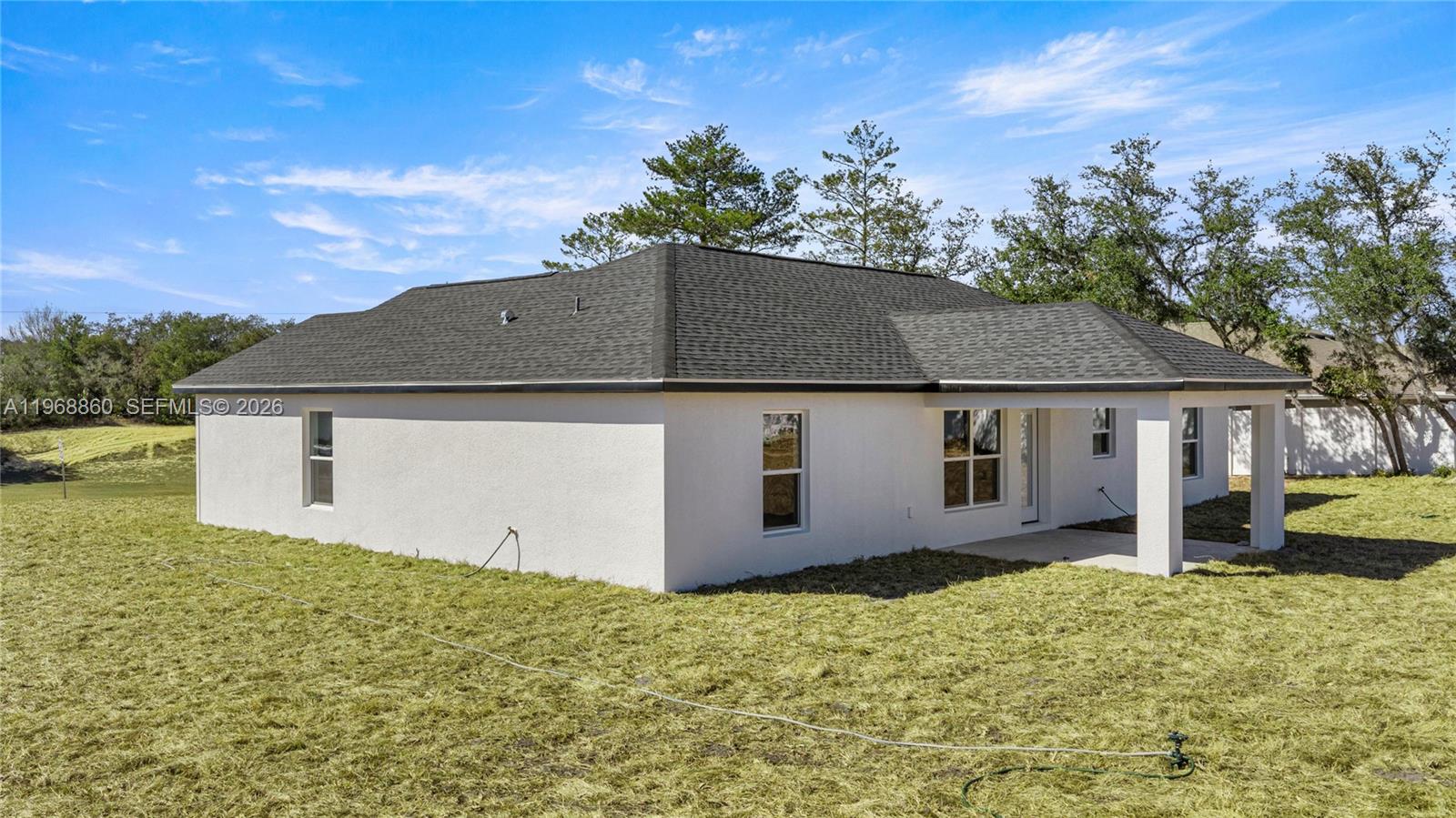 The exterior of a white stucco house features a dark shingled roof and a patio — 9989 SW 42nd Ave, Ocala FL 34476, OCALA, FL