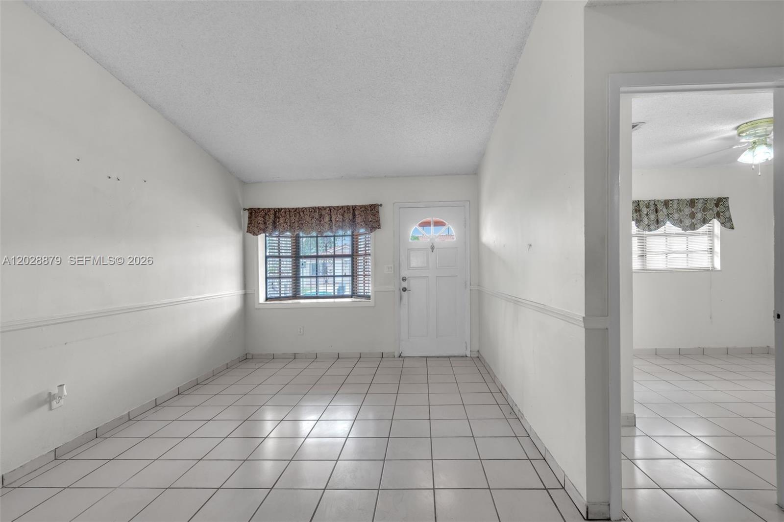 An empty room with white walls, tile flooring, a front door, and a window — 8805 NW 114th Ter, Hialeah Gardens FL 33018, HIALEAH GARDENS, FL