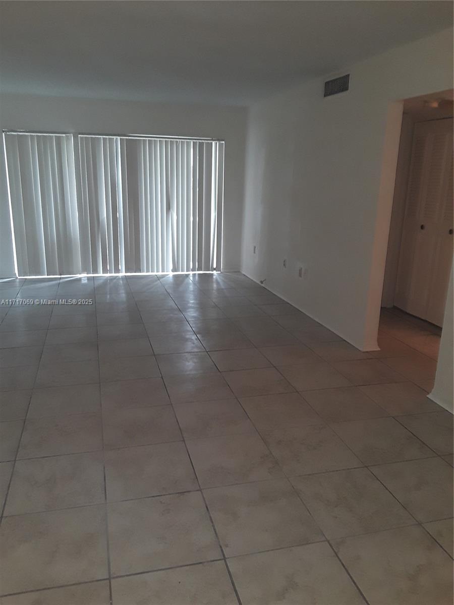 An empty room features white walls, light-colored tile flooring, and large vertical blinds — 8267 SW 128th St # 105, Pinecrest FL 33156, PINECREST, FL