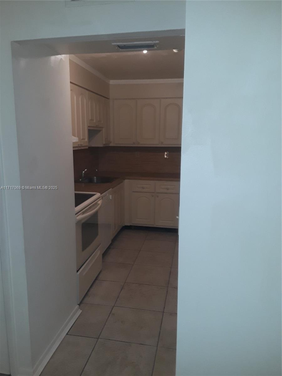 A galley-style kitchen features light-colored cabinetry, a white stove, and beige tile flooring — 8267 SW 128th St # 105, Pinecrest FL 33156, PINECREST, FL