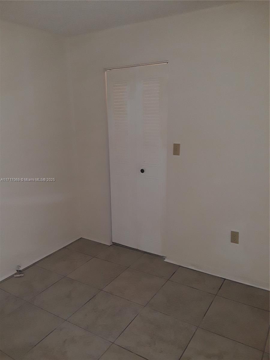 A small, empty room features white walls, a louvered closet door, and tiled flooring — 8267 SW 128th St # 105, Pinecrest FL 33156, PINECREST, FL