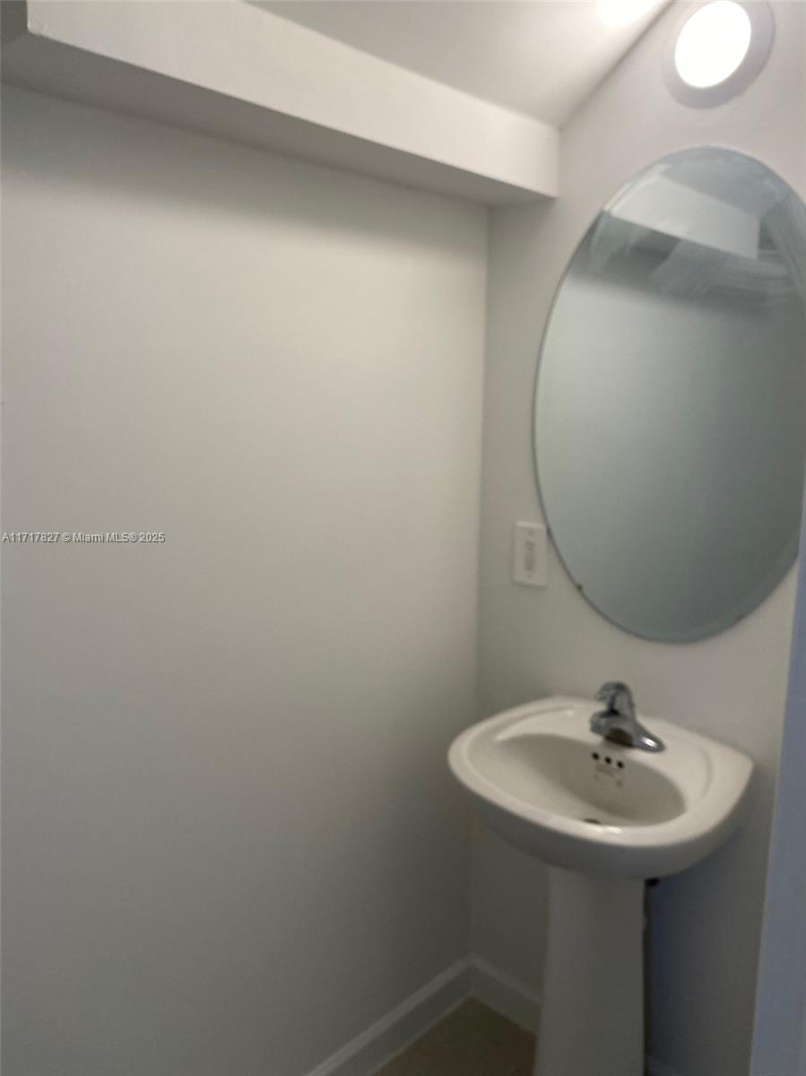 A small bathroom features a white pedestal sink, an oval mirror, and a wall-mounted light — 12623 NW 24th Ave # 12623, Miami FL 33167, MIAMI, FL