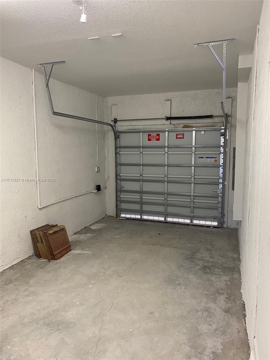 An empty garage features white textured walls, a concrete floor, and a metal sectional door — 12623 NW 24th Ave # 12623, Miami FL 33167, MIAMI, FL