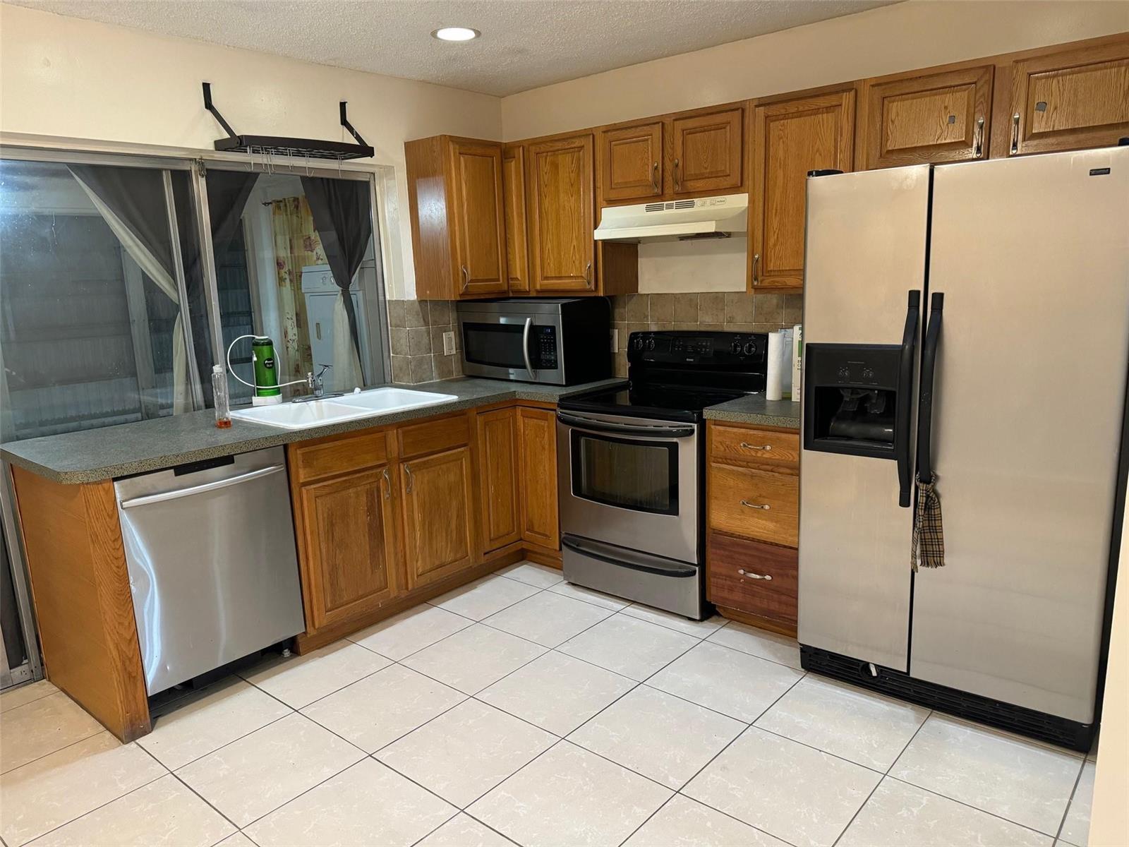 A kitchen features wood cabinets, stainless steel appliances, a double sink, and tiled flooring — 4564 NW 16th Avenue, Tamarac FL 33309, TAMARAC, FL