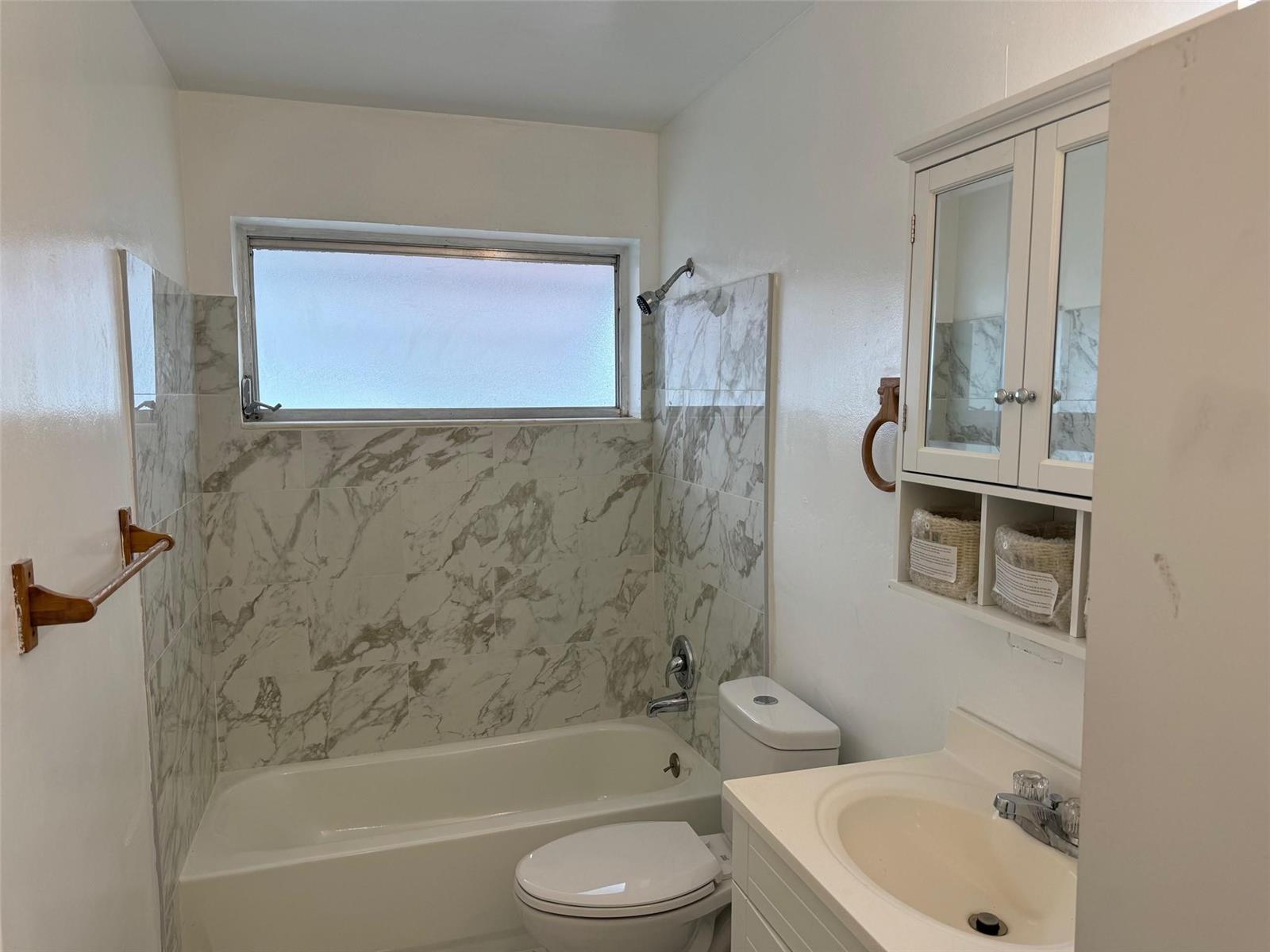A bathroom featuring a white vanity, a toilet, and a bathtub with marble-patterned tile walls — 4564 NW 16th Avenue, Tamarac FL 33309, TAMARAC, FL