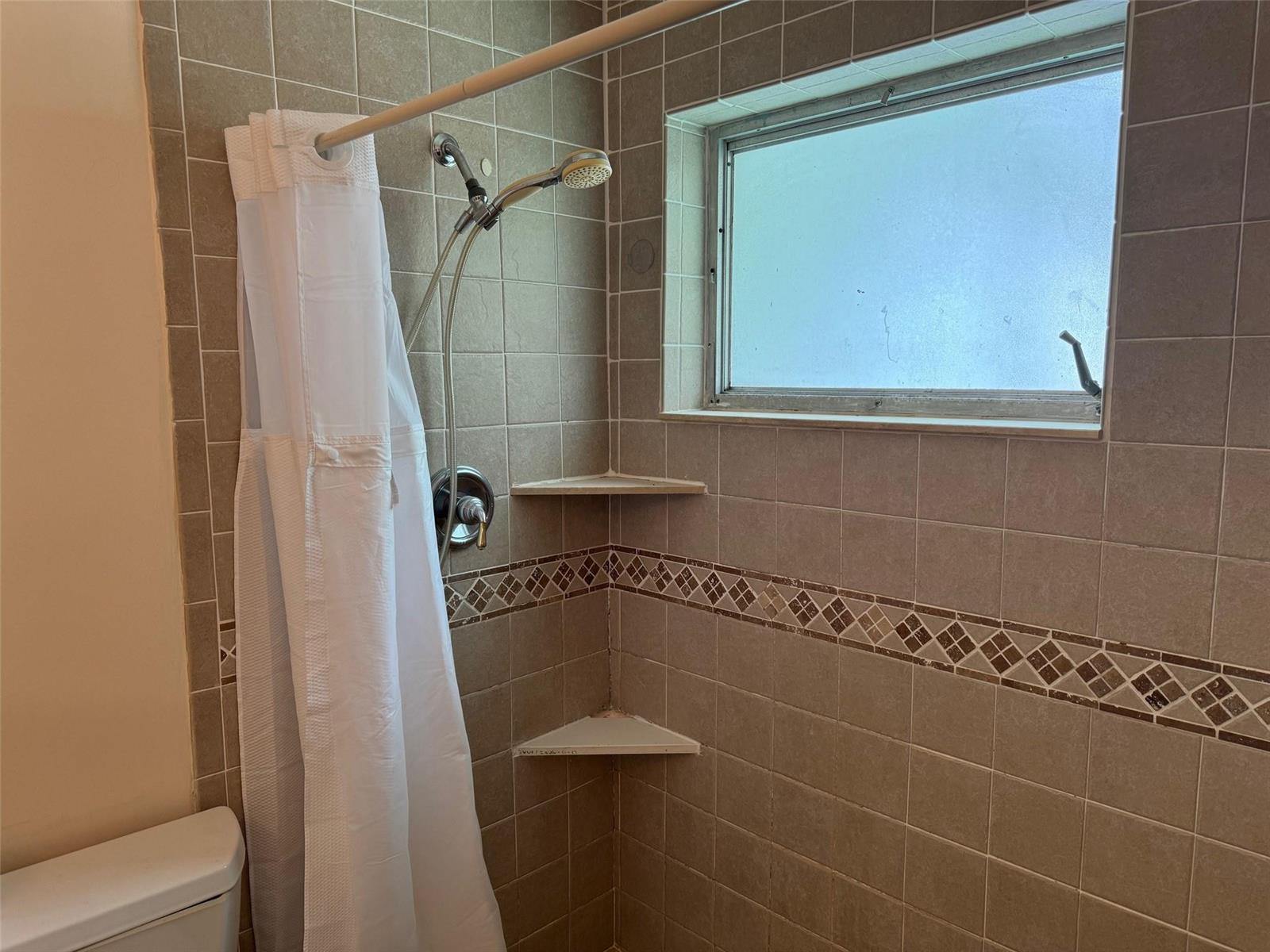 A tiled shower stall features a handheld showerhead, corner shelves, and a frosted window — 4564 NW 16th Avenue, Tamarac FL 33309, TAMARAC, FL