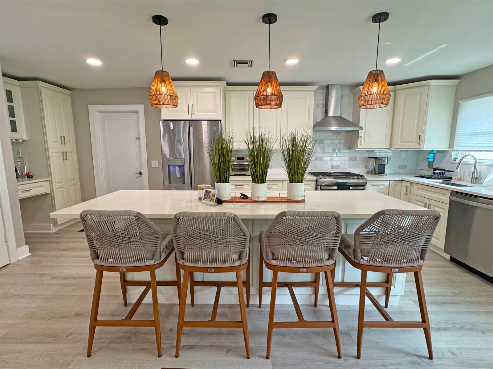 A kitchen features a large white island with four woven barstools and three pendant lights — 106 Periwinkle Drive, Hypoluxo FL 33462, HYPOLUXO, FL