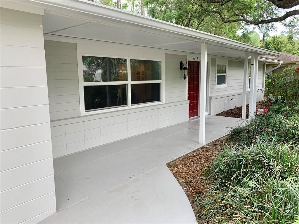 A gray house exterior features a covered porch, a red front door, and large windows — 2219 NW 17TH AVENUE, GAINESVILLE, FL