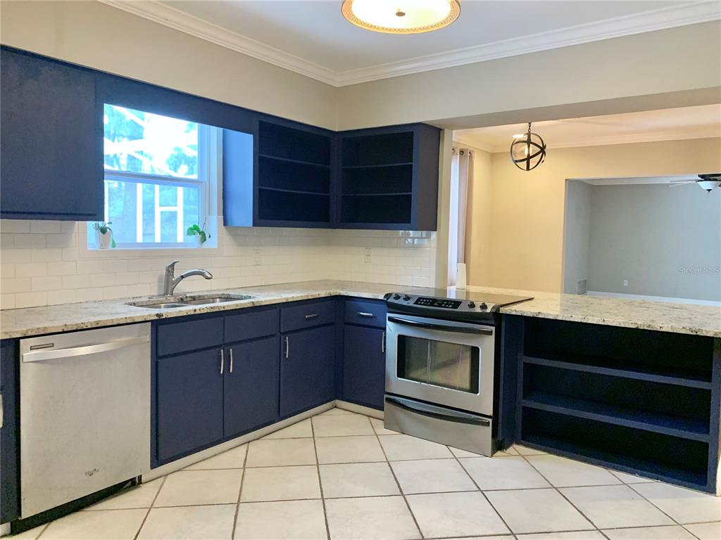 A kitchen features blue cabinets, stainless steel appliances, white tile backsplash, and granite countertops — 2219 NW 17TH AVENUE, GAINESVILLE, FL