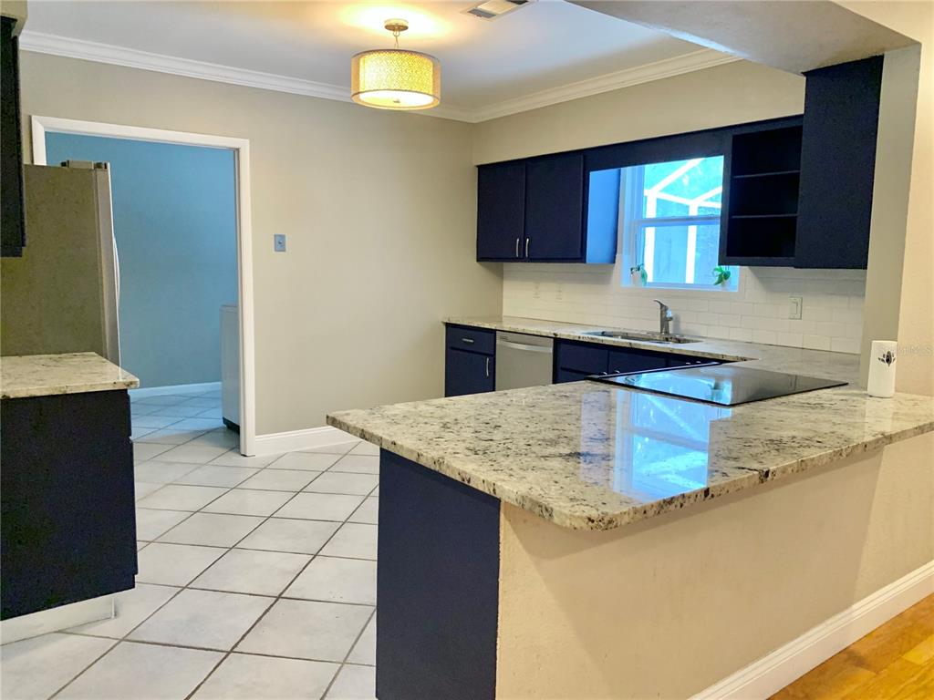 A kitchen features dark blue cabinets, granite countertops, and white tile flooring — 2219 NW 17TH AVENUE, GAINESVILLE, FL