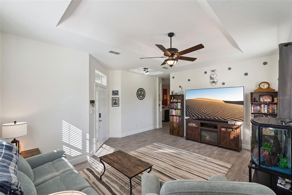 A living room features a tray ceiling, ceiling fan, television on a console, and bookshelves — 2720 SAVANNAH DRIVE, LEESBURG, FL