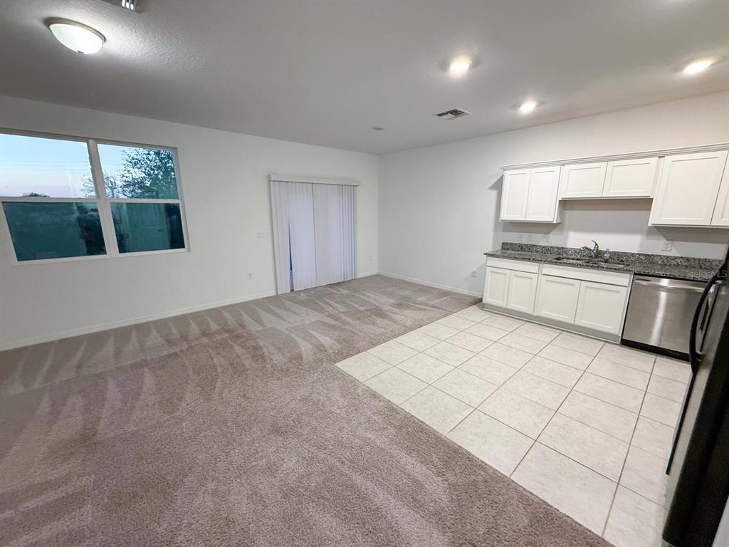 An open-concept room features a carpeted living area, a tiled kitchen, and sliding glass doors — 193 MANDOVI ST, DAVENPORT, FL