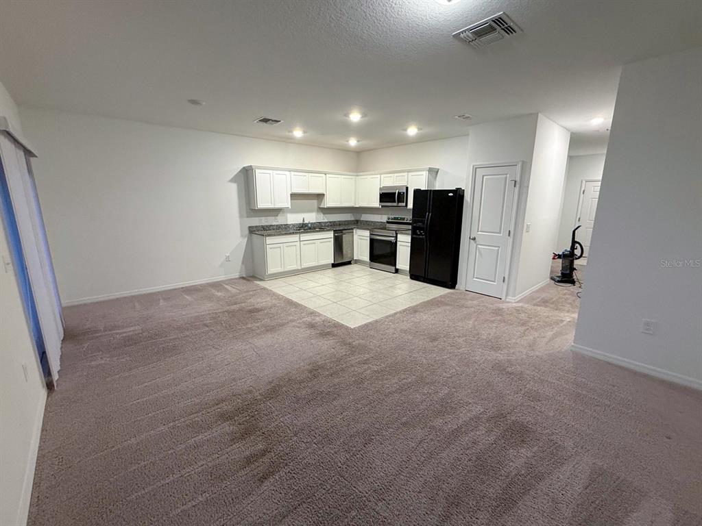 A kitchen with white cabinets and black appliances sits adjacent to a carpeted living area — 193 MANDOVI ST, DAVENPORT, FL