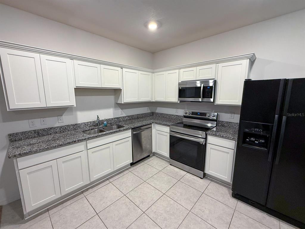 A kitchen features white cabinets, granite countertops, stainless steel appliances, and a black refrigerator — 193 MANDOVI ST, DAVENPORT, FL