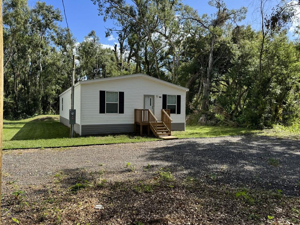 A white single-wide mobile home with a wooden front porch sits on a gravel lot — 9536 MERTON STREET, NEW PORT RICHEY, FL