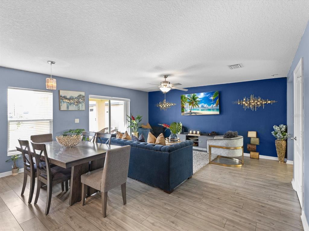 An open-concept living and dining area features blue accent walls, wood-look flooring, and modern furniture — 5372 FEZ COURT, BROOKSVILLE, FL