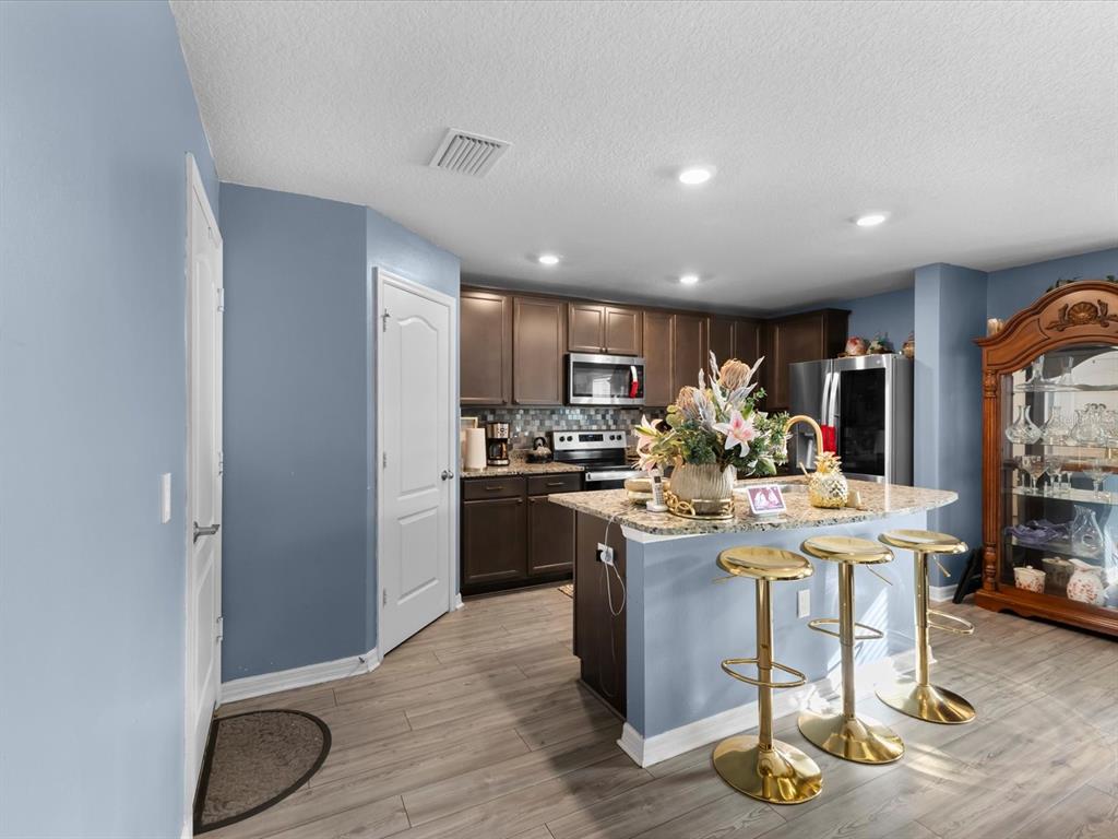 A kitchen features dark wood cabinets, granite countertops, a center island with barstools, and blue walls — 5372 FEZ COURT, BROOKSVILLE, FL