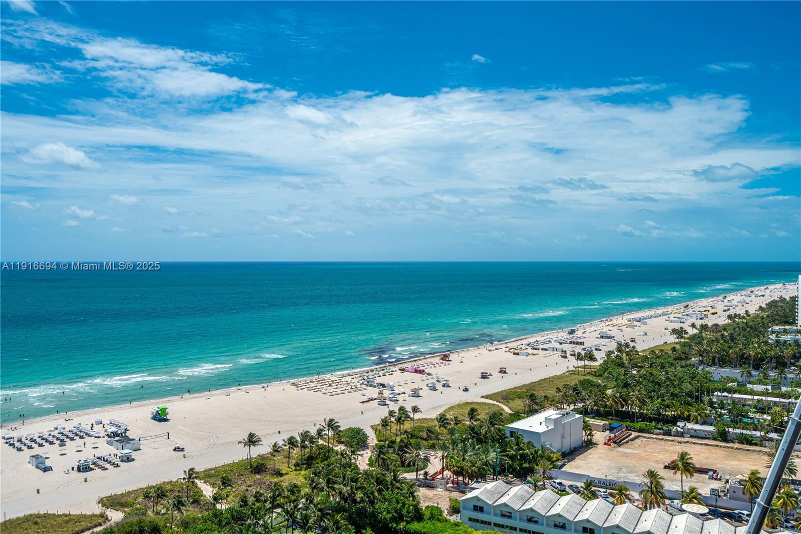 An aerial view shows a sandy beach with umbrellas, palm trees, and the ocean — 101 20th St # 2504, Miami Beach FL 33139, MIAMI BEACH, FL