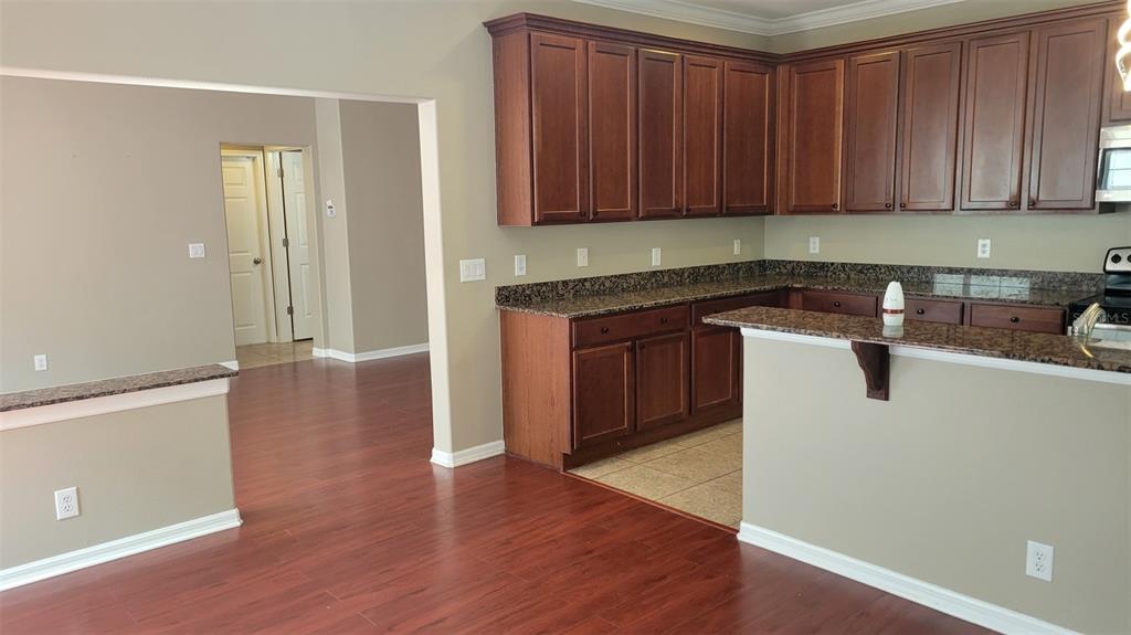 A kitchen with dark wood cabinets, granite countertops, and wood flooring opens to a hallway — 1443 HILLVIEW LANE, TARPON SPRINGS, FL