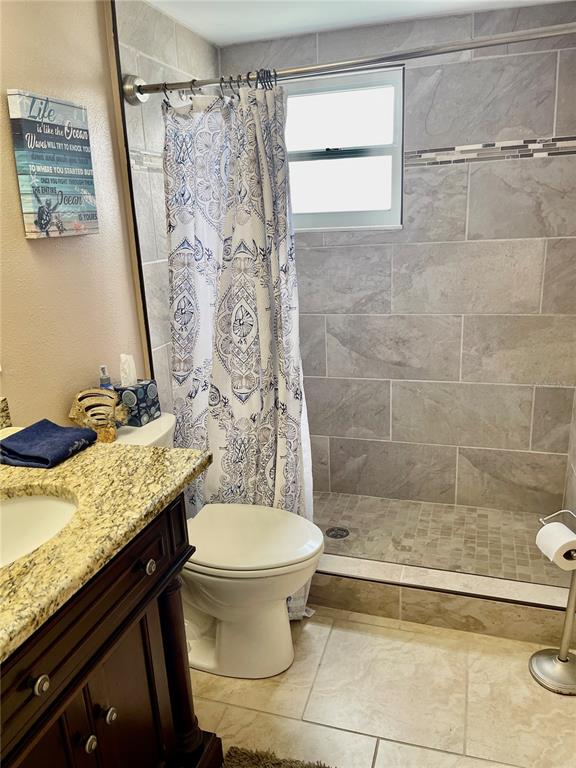 A bathroom features a granite-topped vanity, a toilet, and a tiled walk-in shower — 4650 COVE CIRCLE UNIT 402, ST PETERSBURG, FL
