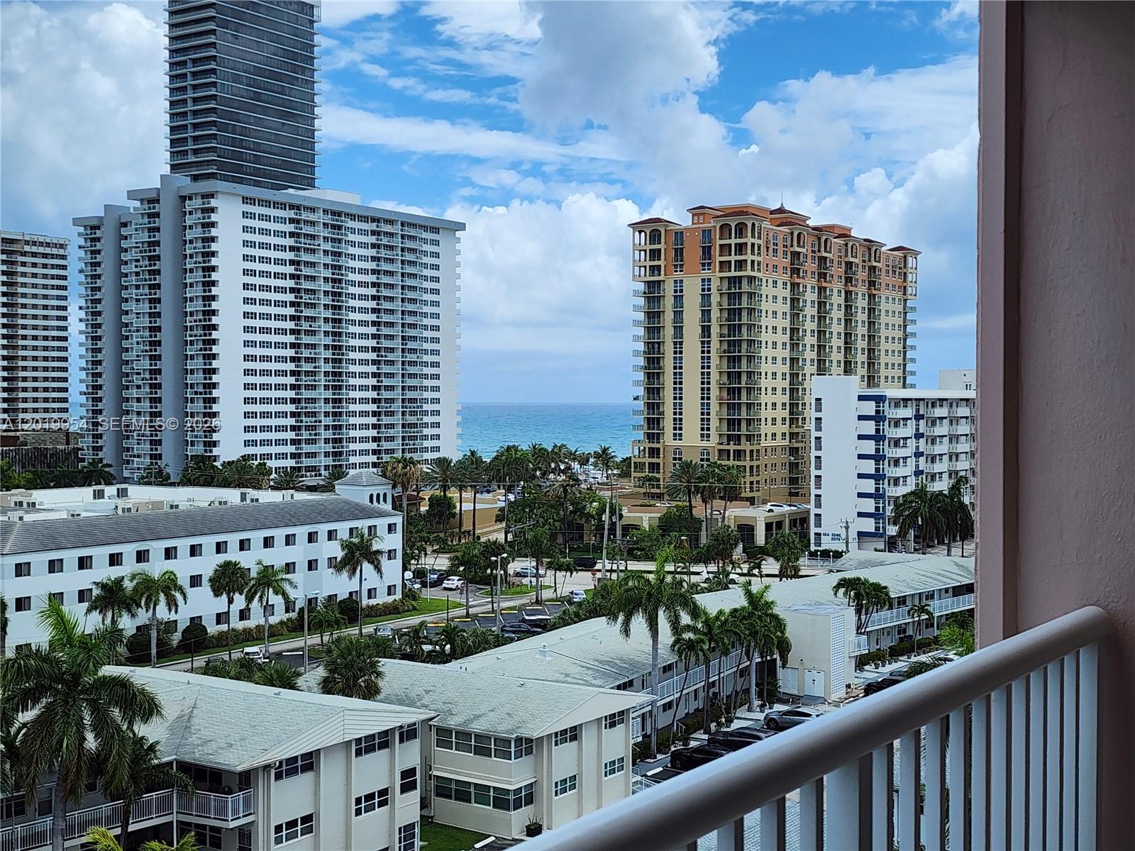 A balcony view overlooks palm trees, low-rise buildings, and high-rise towers near the ocean — 3161 S Ocean Dr # 903, Hallandale Beach FL 33009, HALLANDALE BEACH, FL