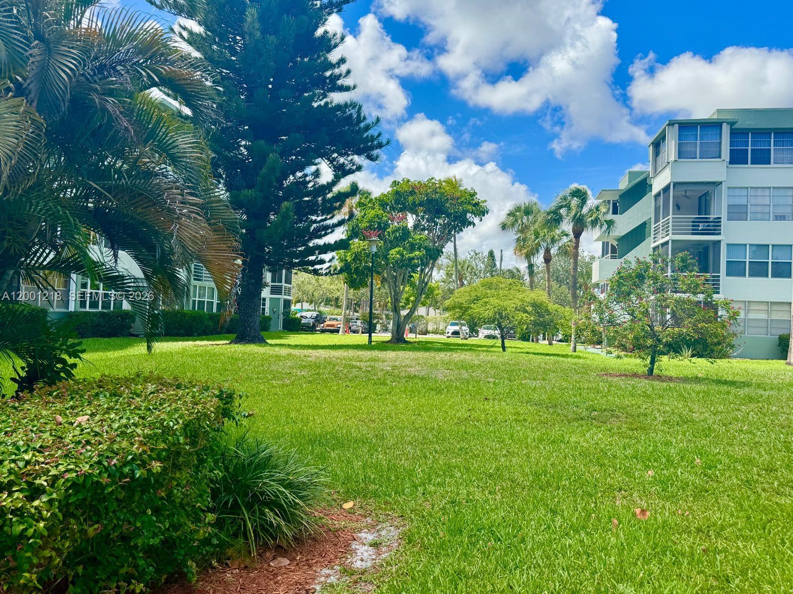 A grassy courtyard sits between two multi-story apartment buildings surrounded by palm trees and landscaping — 2741 Taft St # 404, Hollywood FL 33020, HOLLYWOOD, FL