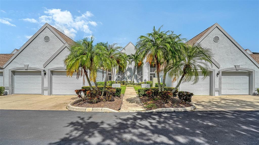 A residential building exterior features four garage doors and a central walkway with palm trees — 6611 STONE RIVER ROAD UNIT 103, BRADENTON, FL
