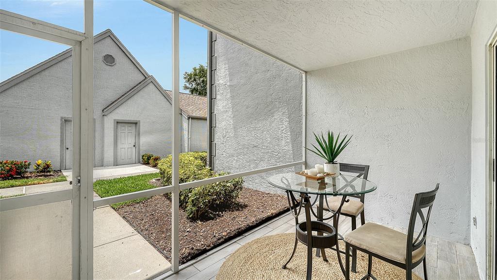 A screened-in patio features a glass-topped table, two chairs, and a view of neighboring buildings — 6611 STONE RIVER ROAD UNIT 103, BRADENTON, FL
