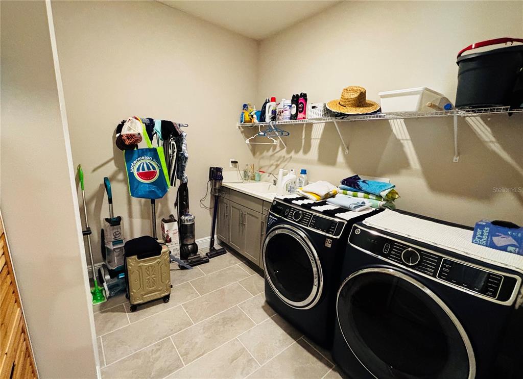 A laundry room features black front-load appliances, gray cabinetry, a utility sink, and tile flooring — 23302 SCAGLIONE DRIVE, LUTZ, FL