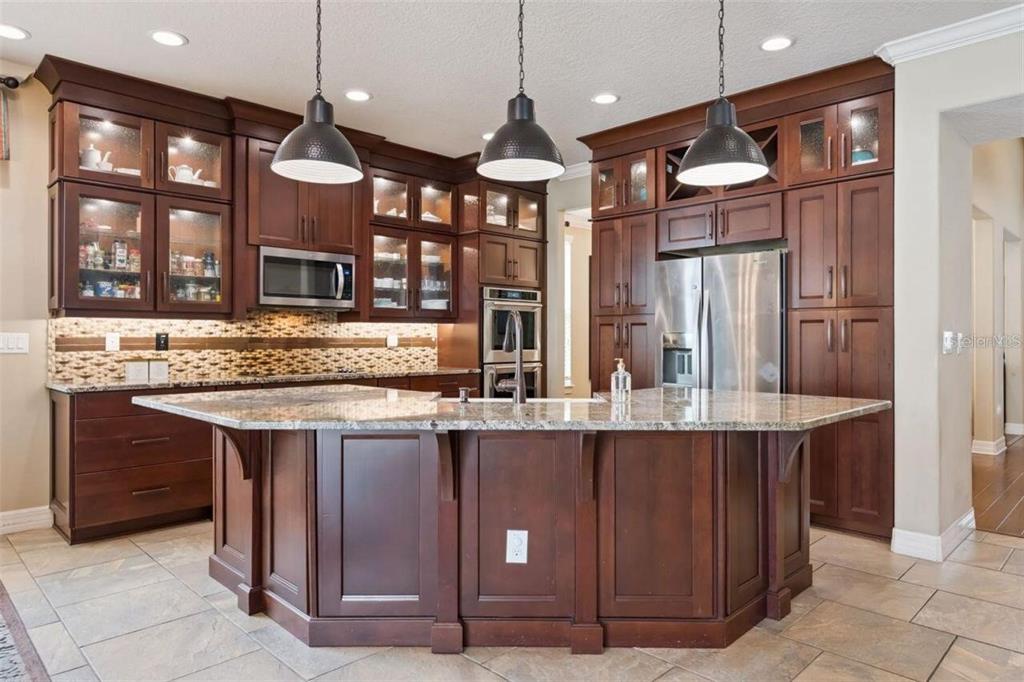 A kitchen with dark wood cabinets, granite countertops, a large island, and stainless steel appliances — 2683 AMATI DRIVE, KISSIMMEE, FL