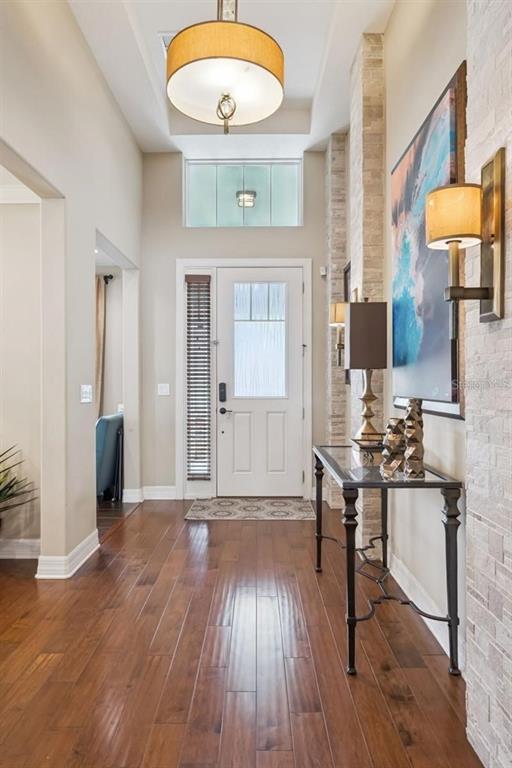 A foyer features hardwood floors, a white front door, a stone accent wall, and lighting — 2683 AMATI DRIVE, KISSIMMEE, FL